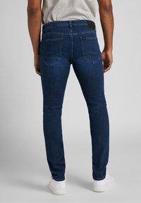 Dark blue, slim-fit jeans with a classic five-pocket design and visible stitching. Features a branded waist patch and subtle fading.