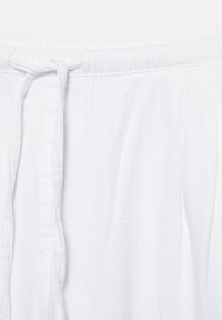 Pantaloni albi din bumbac cu talie elastică și șnur legat în față, evidențiind detaliile texturii materialului.