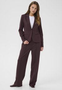 Completo bordeaux con giacca aderente e pantaloni dritti, realizzato in un tessuto liscio; presenta tasche piatte e chiusura con bottoni.
