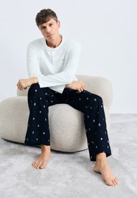 Chemise blanche à manches longues avec un col Henley, associée à un pantalon de pyjama bleu marine orné d'un motif circulaire coloré. Tissu doux et coupe décontractée.