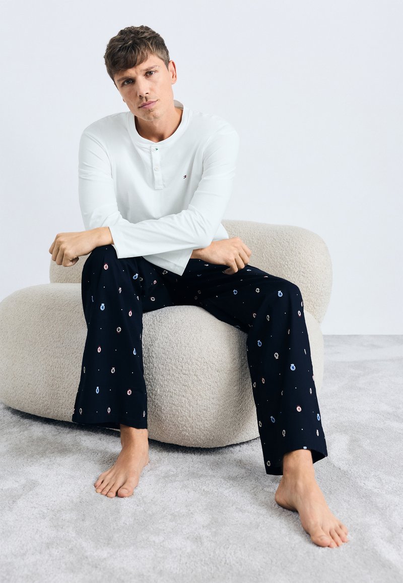 Chemise blanche à manches longues avec un col Henley, associée à un pantalon de pyjama bleu marine orné d'un motif circulaire coloré. Tissu doux et coupe décontractée.
