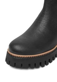 Boots de glezne din piele neagră, cu vârf rotund, având o talpă groasă din cauciuc negru, cu un margine texturată și o bordură subtilă de culoare marron.