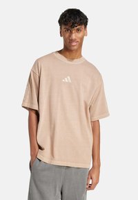 Light beige oversized t-shirt made of cotton, featuring a round neck and short sleeves, with three vertical stripes on the shoulders and a logo.