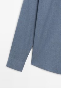 Světle modrá, texturovaná košile s dlouhým rukávem, zaobleným lemem a manžetami na knoflíky, s jemným vzorem tkaniny.