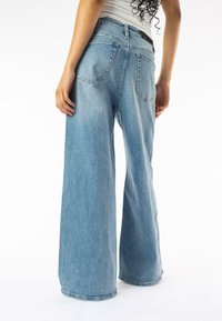 Jean large bleu clair en denim, avec taille haute, deux poches arrière et un ourlet net. Coutures visibles et coupe décontractée.