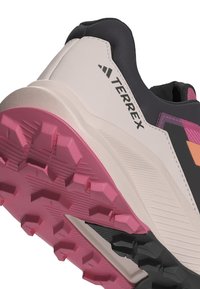 Zapatillas Terrex que presentan una suela de goma con tacos de tracción rosa, parte superior beige con acentos negros y un diseño texturizado para mayor agarre.
