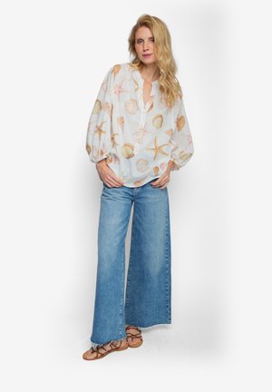 Lekka, przezroczysta biała bluzka z nadrukiem muszelek i rozgwiazd. Posiada luźny krój, plisę na guziki oraz bufiastymi rękawami. Dopasowana do szerokich dżinsów z rozszerzanymi nogawkami.