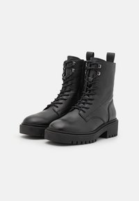 Pair of black leather lace-up ankle boots with chunky rubber soles and side zippers on a white background.