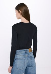 Schwarzes Langarmoberteil mit rundem Halsausschnitt, kombiniert mit hellblauen, hoch taillierten Jeans, die ein quadratisches Rückenkleidungsstück und Gesäßtaschen aufweisen.