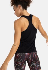 Czarna tank topka z designem racerback, z złotym akcentem na ramieniu. Noszona z kolorowymi, kwiatowymi legginsami.