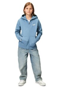 Blå zip-hoodie med framficka och logotyp. Matchad med ljusblå snittiga jeans och vita sneakers. Har en huva och ribbade ärmslut.