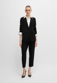 Czarny garnitur skrojony na miarę z dopasowaną marynarką, białą koszulą i zwężanymi spodniami. Posiada gładką teksturę i ostre kołnierz z pojedynczym zapięciem na guzik.