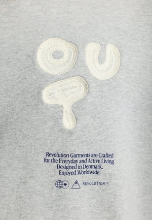 Grijze sweatshirt met textuur in crèmekleurige borduurwerk met de letters "ou" en een cirkelvormig ontwerp. Inclusief blauwe gedrukte tekst onderaan.
