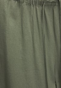 Tissu vert olive à texture douce, doté d'une taille élastique et d'un cordon de serrage. Le matériau semble léger et légèrement froissé.