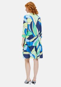 Bunt gemustertes Kleid mit kurzen Ärmeln, geraffter Taille und einem gestuften Rock. Schattierungen von Blau, Grün und Marineblau mit einem abstrakten Blätterdesign.