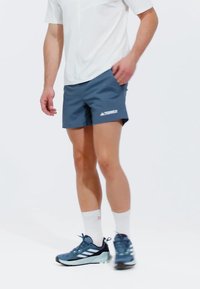 Blå sportshorts med logotyp, kombinerat med en vit skjorta och blå löparskor. Designen är lätt och har en avslappnad passform.