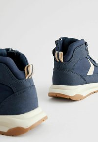 Chaussures de randonnée marine avec tige en textile, semelle en caoutchouc et accents beiges. Présente une surface texturée et une languette de traction au niveau du talon.