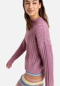 Pink ribbed sweater with a fitted design, long sleeves, and textured knit. Paired with a multicolored striped skirt featuring horizontal lines.