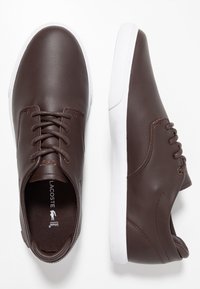Baskets en cuir marron à texture lisse, semelles en caoutchouc blanc et design classique à lacets. Présente un marquage discret sur la languette.