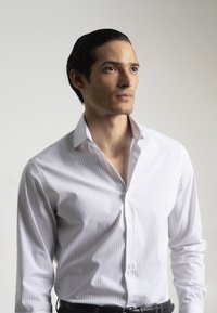 Camisa de vestir blanca con delgadas rayas verticales, cierre frontal de botones, cuello extendido y diseño ajustado. Tejido suave con un ligero brillo.