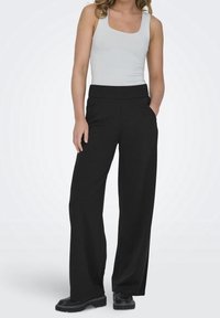 Black wide-leg trousers with a smooth texture, featuring a high waistband and side pockets, paired with a light gray fitted tank top.