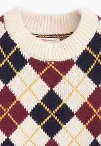 Pull tricoté présentant un motif losanges en bordeaux, marine, crème et jaune. Encolure ronde avec bord-côte et tissu texturé.