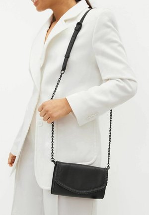 Sac à bandoulière en cuir noir avec un rabat avant tressé et une bandoulière en chaîne, présentant une surface texturée et une forme rectangulaire compacte.