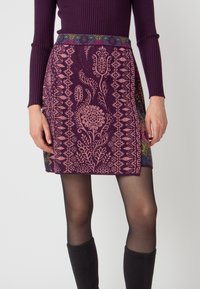 Knit mini skirt in dark purple with pink floral patterns, complemented by a textured, multicolored waistband. Tight-fitting with side accents.