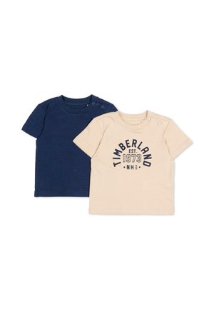 Twee baby-T-shirts, één effen donkerblauw en één beige met de tekst "Timberland EST. 1973 NH USA", beide met drukknoopjes op de schouders.