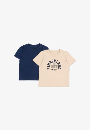 Two baby t-shirts, one navy blue plain and one beige with "Timberland EST. 1973 NH USA" text, both with shoulder snap buttons.