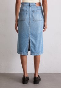 Lichtblauwe denim midi rok met zichtbare stiksels, een centrale rugsplit en twee achterzakken. Leren logo patch op de tailleband.