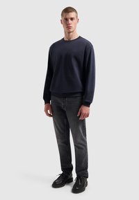 Marine sweatshirt met een ronde halslijn en geribde manchetten, gecombineerd met donkere jeans en zwarte schoenen, met een subtiele logo op de borst.