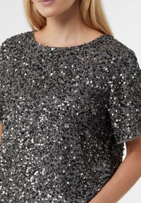 Graues Paillettentop mit lockerem, kastigem Schnitt und rundem Ausschnitt. Verziert mit zahlreichen schimmernden silbernen Pailletten auf einem weichen Stoff.
