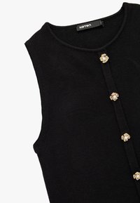 Top negro sin mangas hecho de una tela suave, con un cuello redondo y botones con detalles en oro y perlas en el frente.