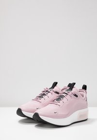 Rosa Nike-sneakers med en slät textilöverdel, svarta detaljer, snörningsdesign, dämpad sula och synlig luftkudde i klacken.