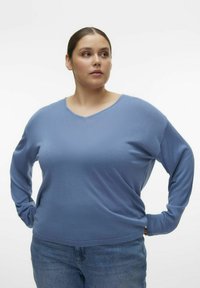 Top a maniche lunghe azzurro chiaro con scollatura a V e vestibilità rilassata. Tessuto morbido e design leggermente largo, abbinato a jeans in denim di lavaggio medio.