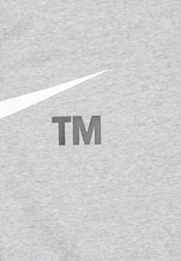 Šedá mikina s velkým bílým logem Nike a tmavě šedým označením „TM“, vyrobená z měkké, texturované látky.