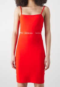 Czerwona bawełniana sukienka o dopasowanym kroju, na cienkich ramiączkach, z paskiem z logo Calvin Klein Jeans w pasie. Prosty design, gładka faktura.