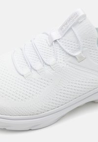 Baskets blanches avec une tige en mesh texturé, un design élégant, des lacets élastiques et une semelle extérieure blanche lisse. Présentent un accent subtil gris clair.