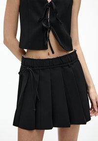 Schwarzes Cropped-Top mit Bindeschluss, kombiniert mit einem schwarzen plissierten Rock mit elastischem Bund und verstellbarem Kordelzug.