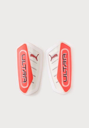 Par de espinilleras Puma Ultra Flex blancas y rojas con el logo de Puma y la marca Ultra Flex sobre un fondo liso.