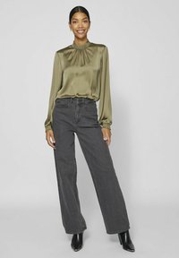 Olivgrön satinklänning med volangkrage, matchad med högmidjade, vida mörkgrå jeans och eleganta svarta klackstövlar.