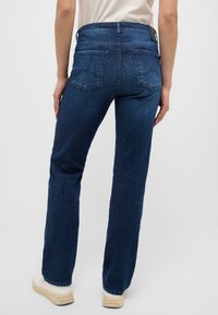 Jeans de mezclilla azul oscuro con un diseño de pierna recta. Presenta dos bolsillos traseros y una etiqueta en la cintura. Textura suave, hardware mínimo.
