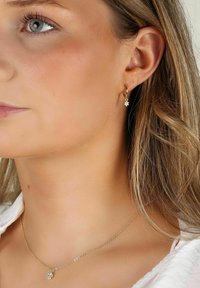 Guldörhängen med en liten blomma hängande och ett matchande guldhalsband med en liknande blomstercharm. Slät, glänsande yta.