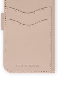 Tarjetero de cuero beige con dos ranuras curvas para tarjetas y "IDEAL OF SWEDEN" grabado en el centro inferior.