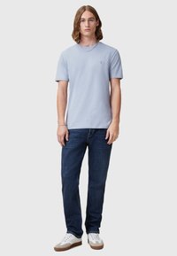 Light blue short-sleeve t-shirt with crew neckline, paired with dark blue jeans and gray-accented white sneakers. Simple design with logo detail.