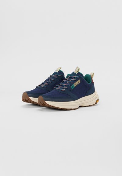 Des baskets bleu marine avec une tige en mesh, des lacets multicolores, une semelle intermédiaire beige et une semelle extérieure en caoutchouc texturé. Présente une étiquette d'accent vert.