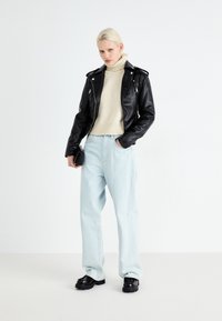 Black leather motorcycle jacket over a cream turtleneck, paired with light blue wide-leg jeans and black platform shoes. Simple clutch in hand.