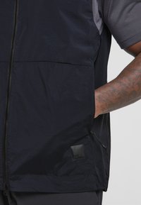 Marineweste aus leichtem, ripstop Material mit einem vollständigen Reißverschluss und Seitentaschen. Mit einem kleinen schwarzen Logo-Patch auf der unteren linken Seite.