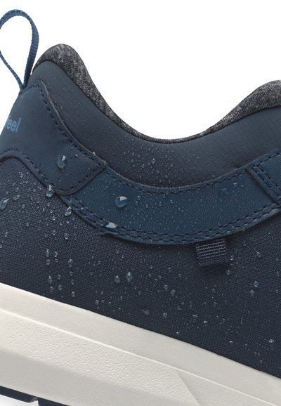 Blue sneaker with a textured surface, water droplets visible, padded collar, and beige rubber sole. Features a rear pull tab for easy wear.